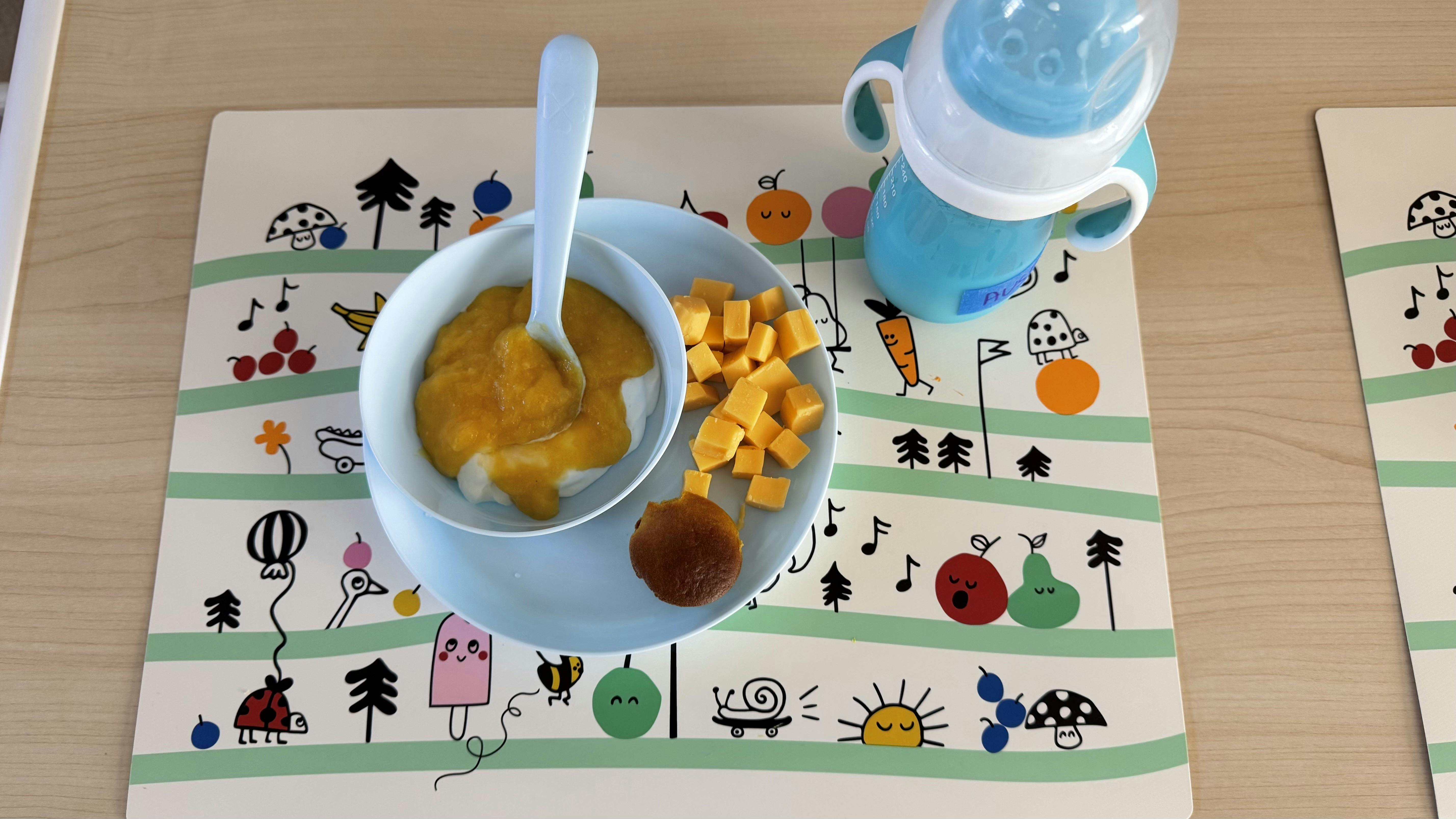 Baby food bowl with spoon, diced food, and sippy cup on a placemat