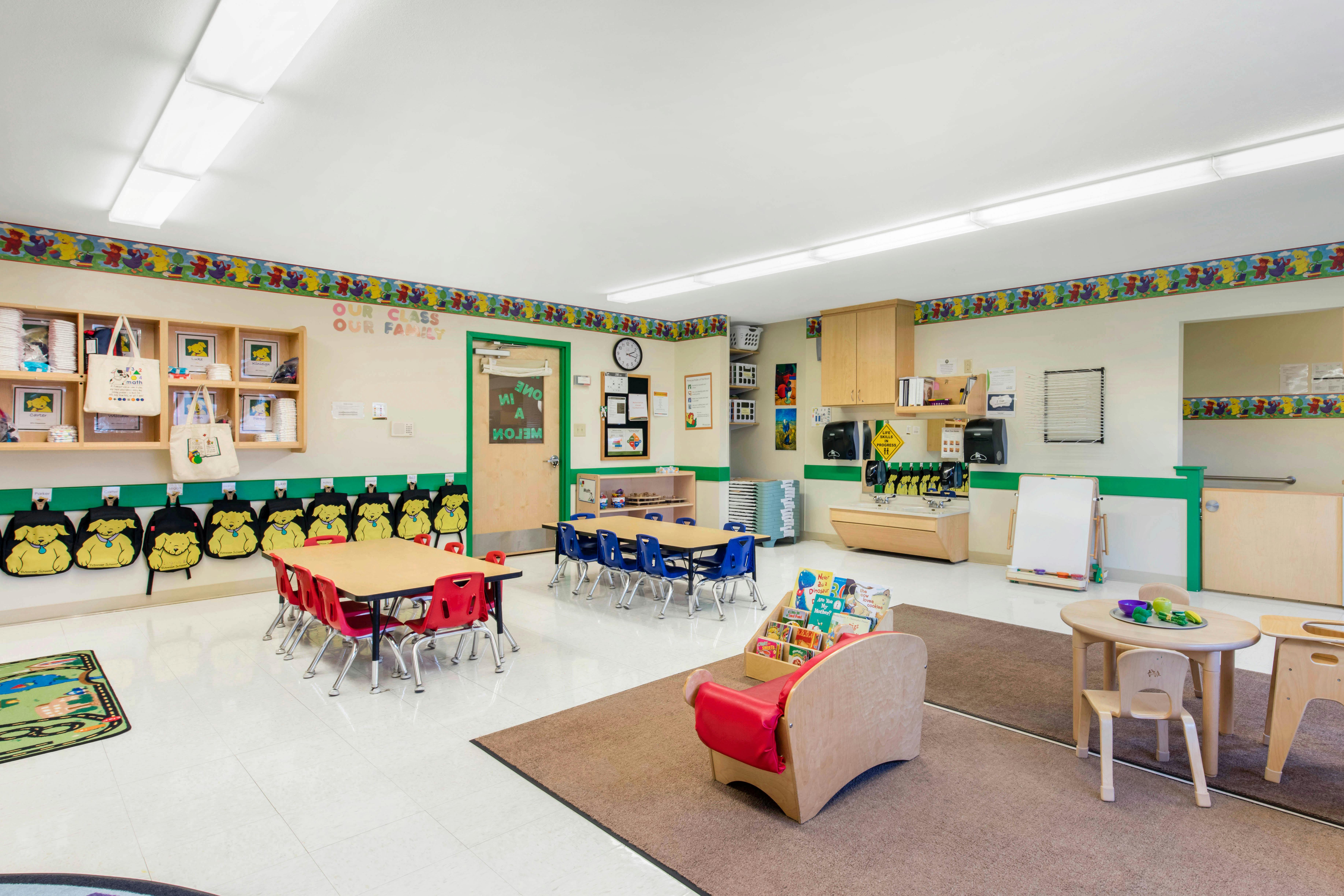 Classroom with tables and chairs, cubbies, sink, whiteboard, and book display