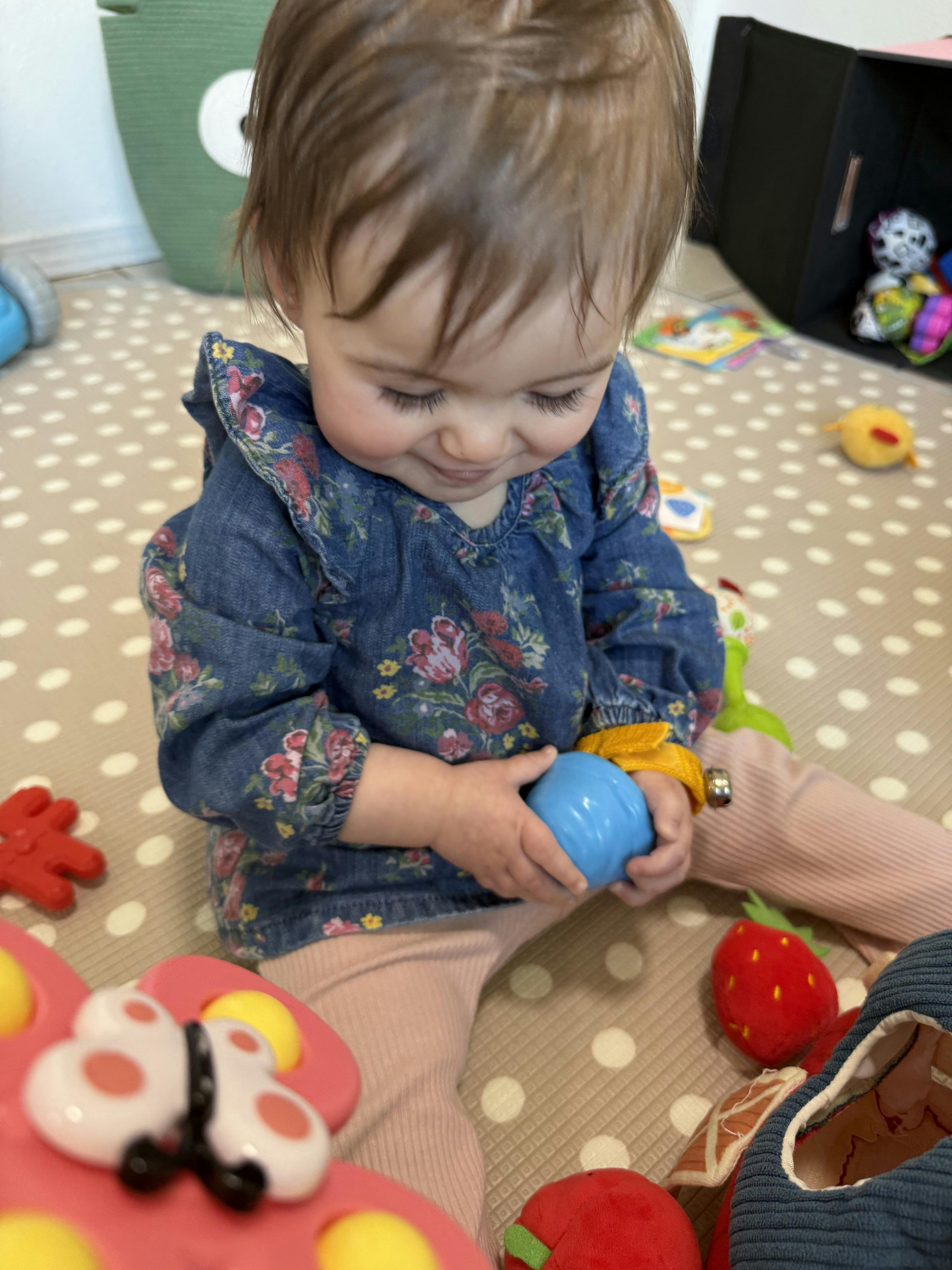 Child sitting on a playmat, holding a blue ball