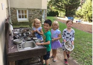 Four children playing with a mud kitchen outdoors