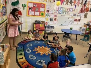 Adult standing in classroom with children sitting on a rug