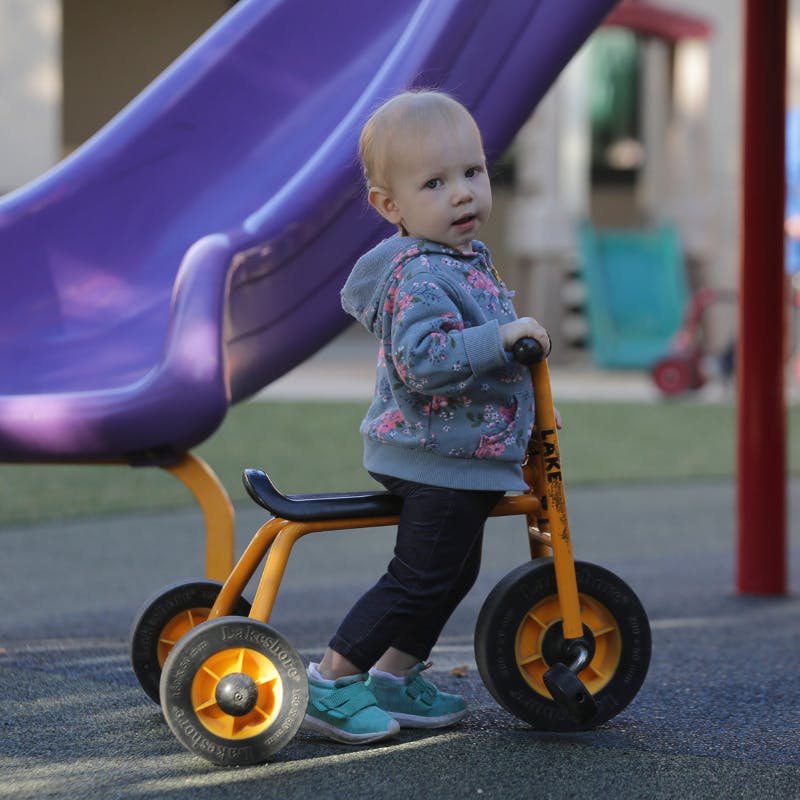 Child on a tricycle next to a purple slide