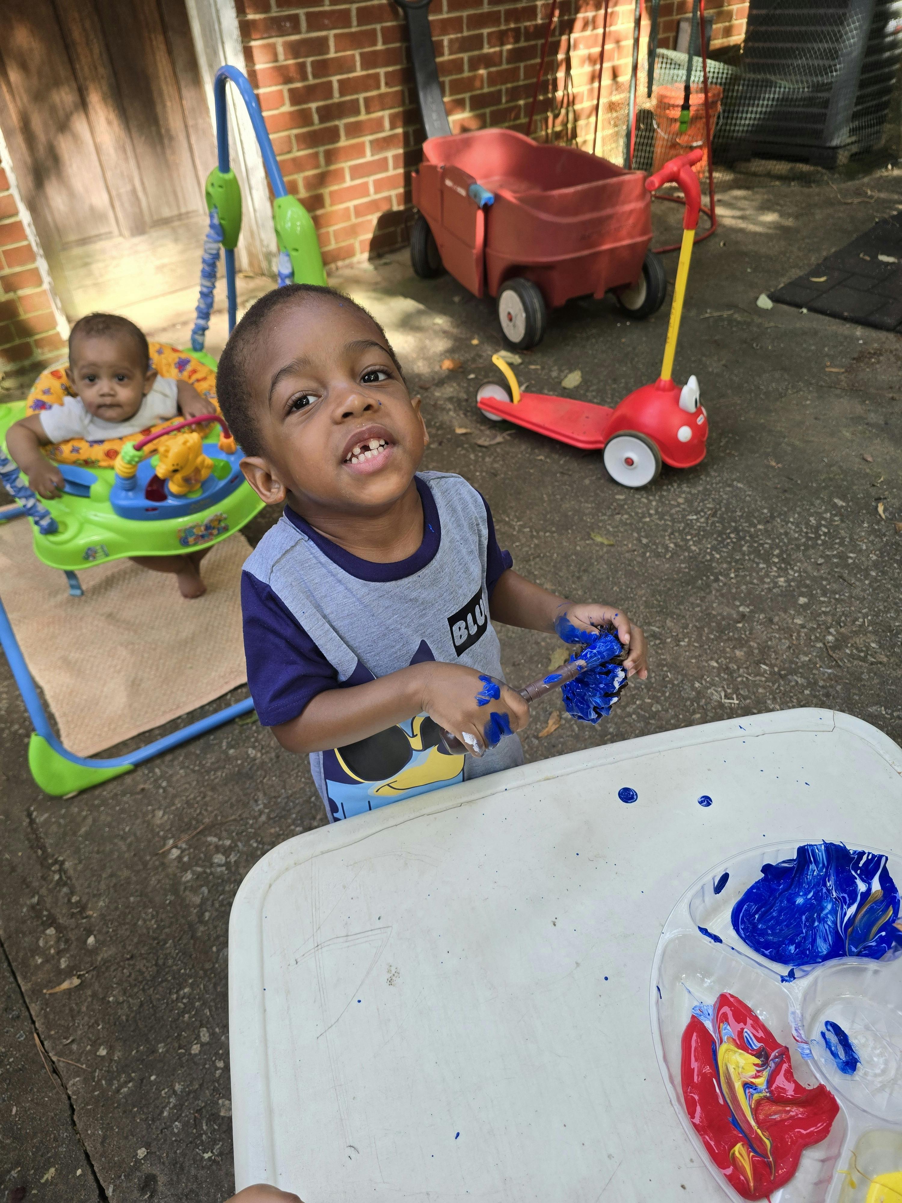 Child painting with blue paint, another child in a baby bouncer in the background