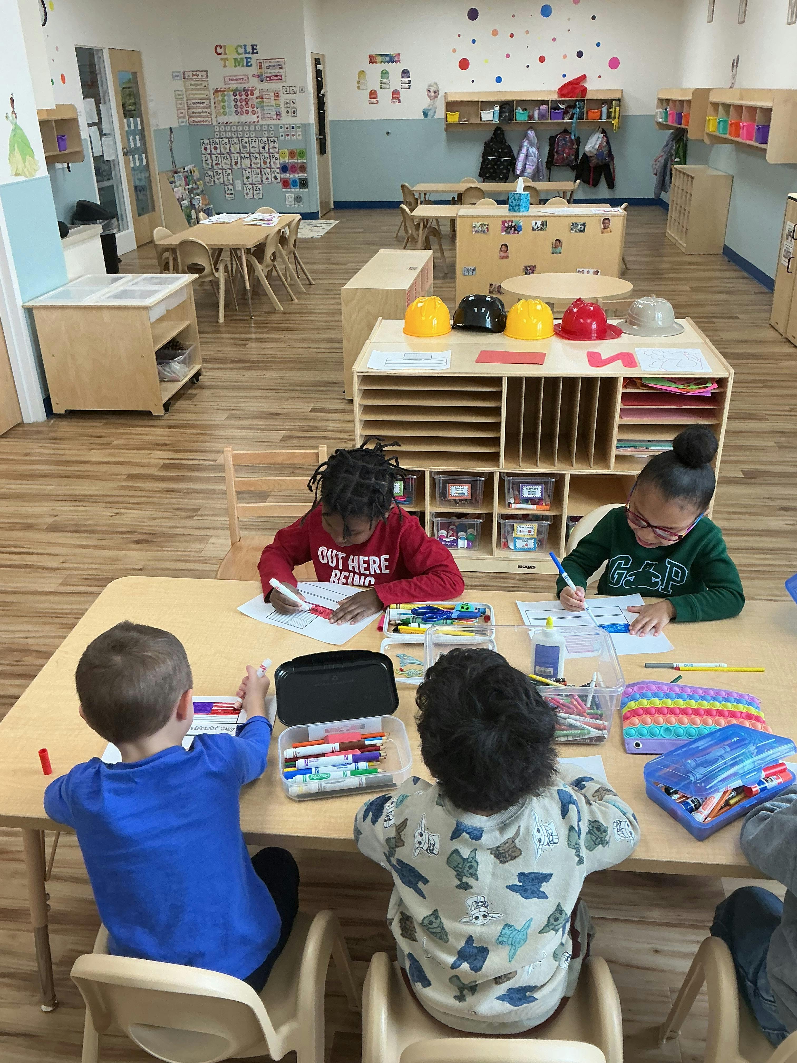 Four children drawing and coloring at a classroom table