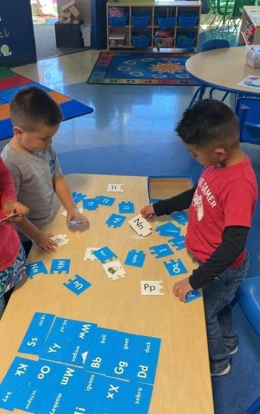 Two children playing with alphabet letter puzzles at a table