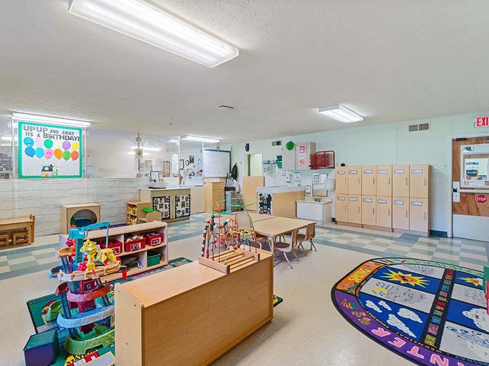 Playroom with small tables, storage units, toys, and a birthday banner