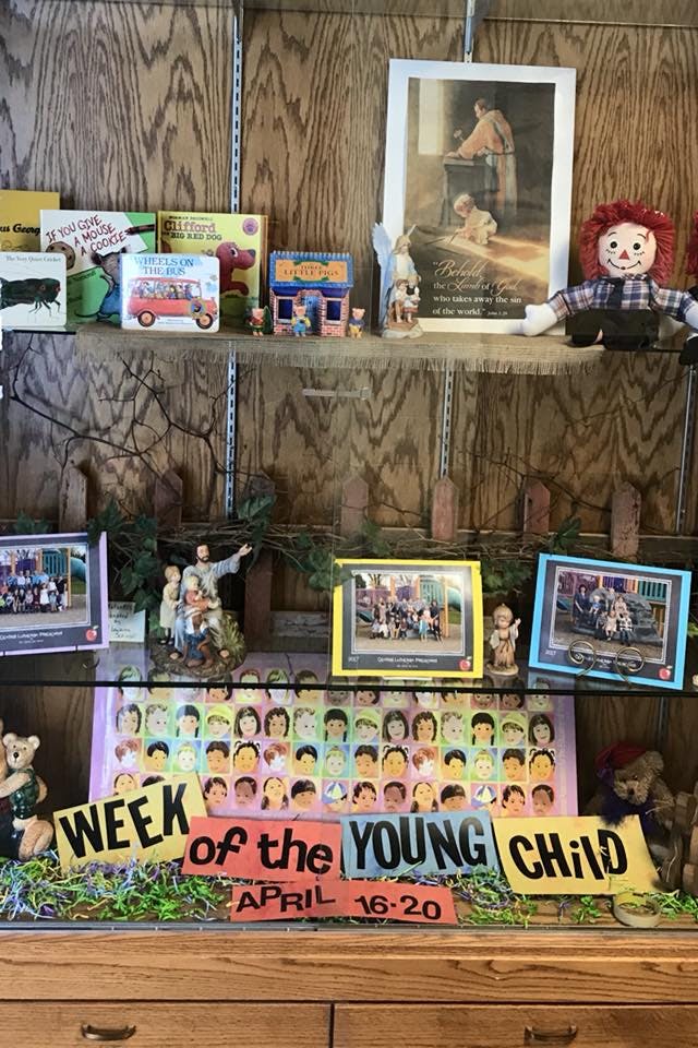Shelf with books, framed pictures, and a "Week of the Young Child" sign