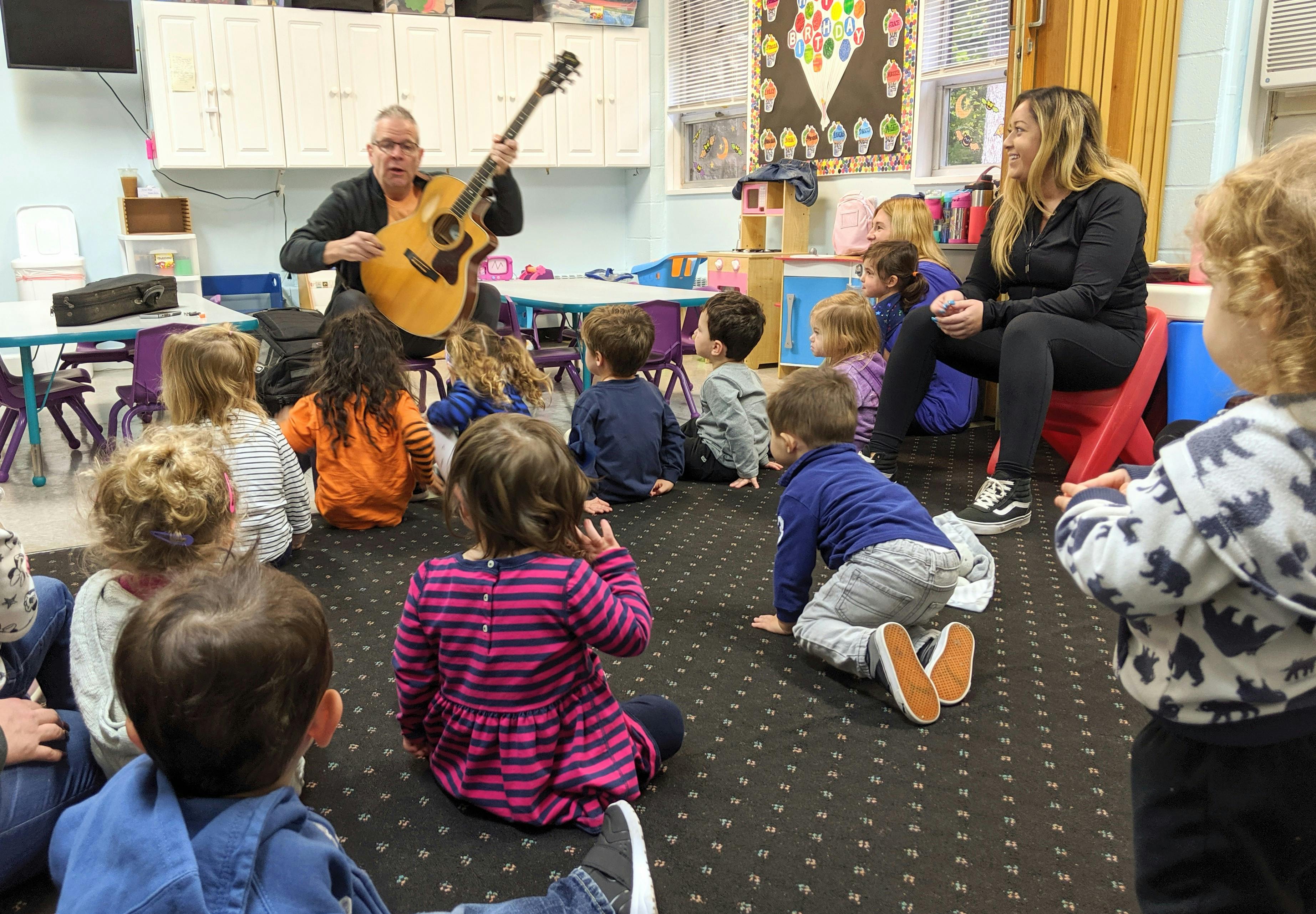 Person playing guitar for a group of children in a classroom