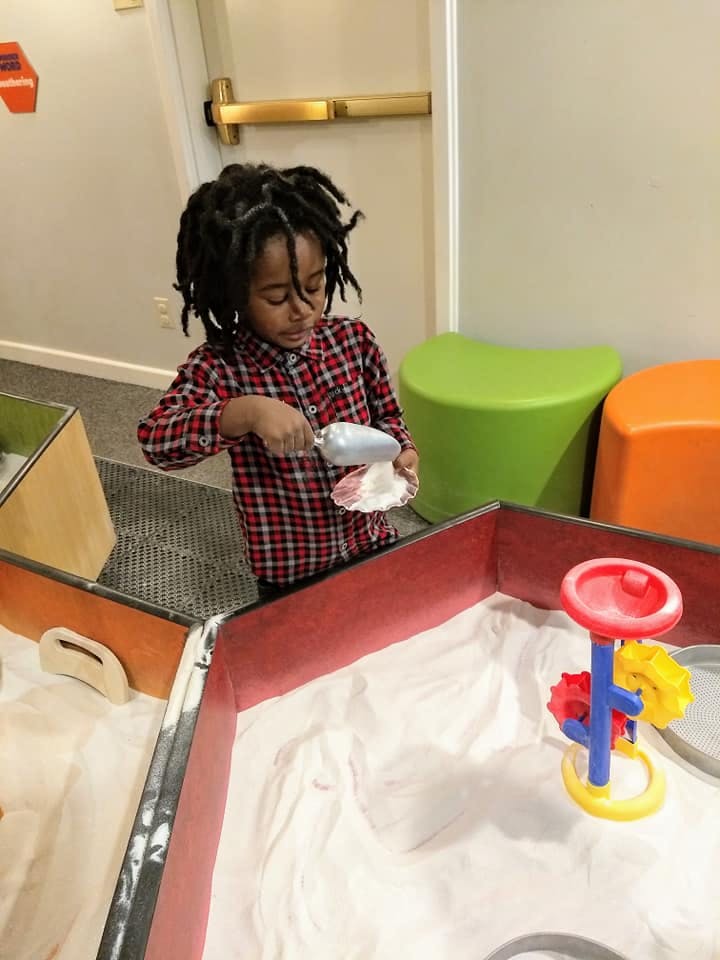 Child playing in a sand table with a scoop and shell