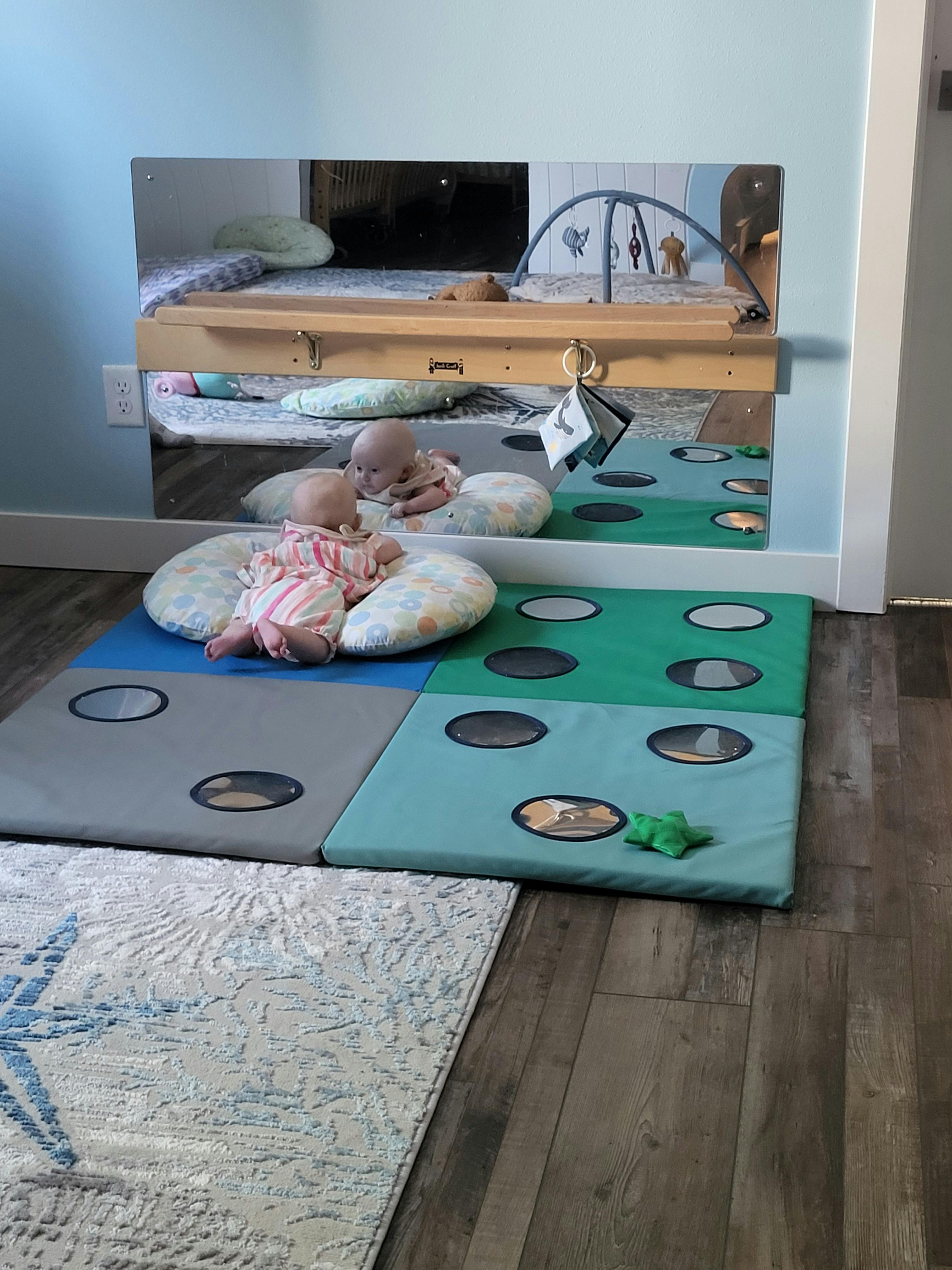 Two infants lying on soft pillows on a play mat with mirrors