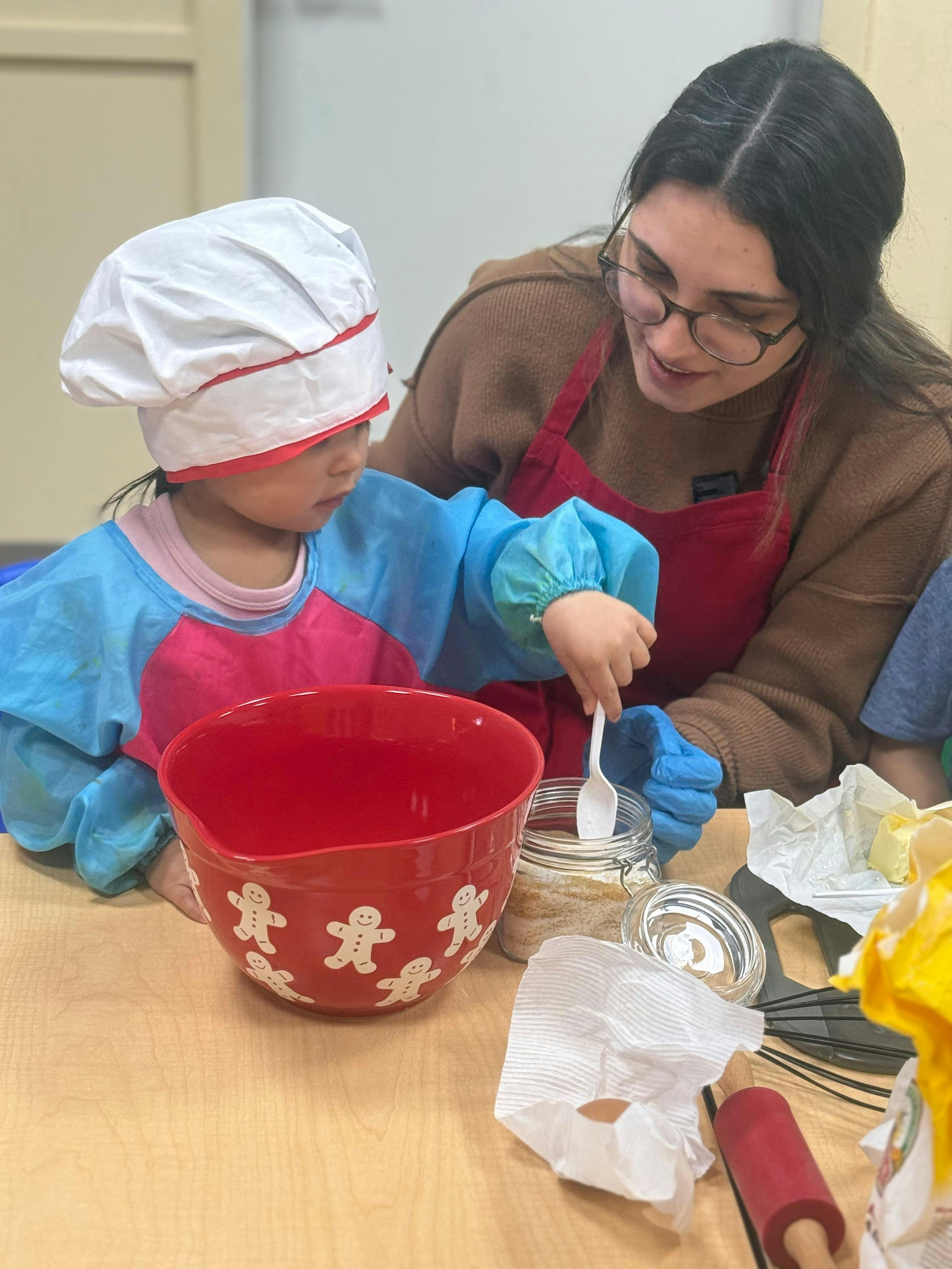 Child wearing a chef hat baking with an adult