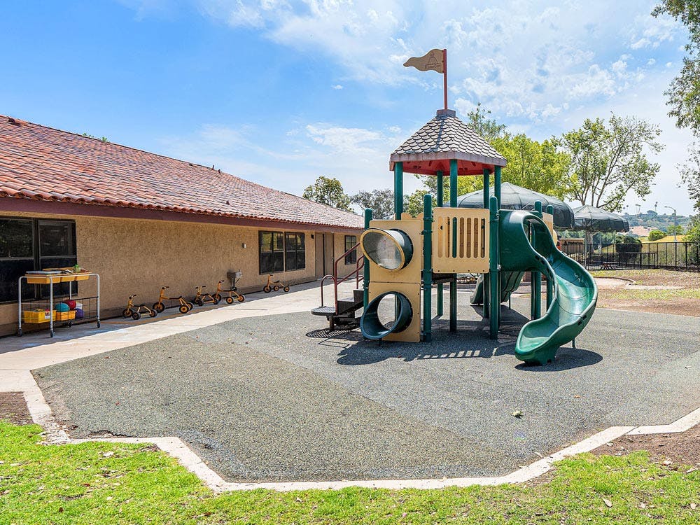 Playground structure with slides next to a building with small bikes