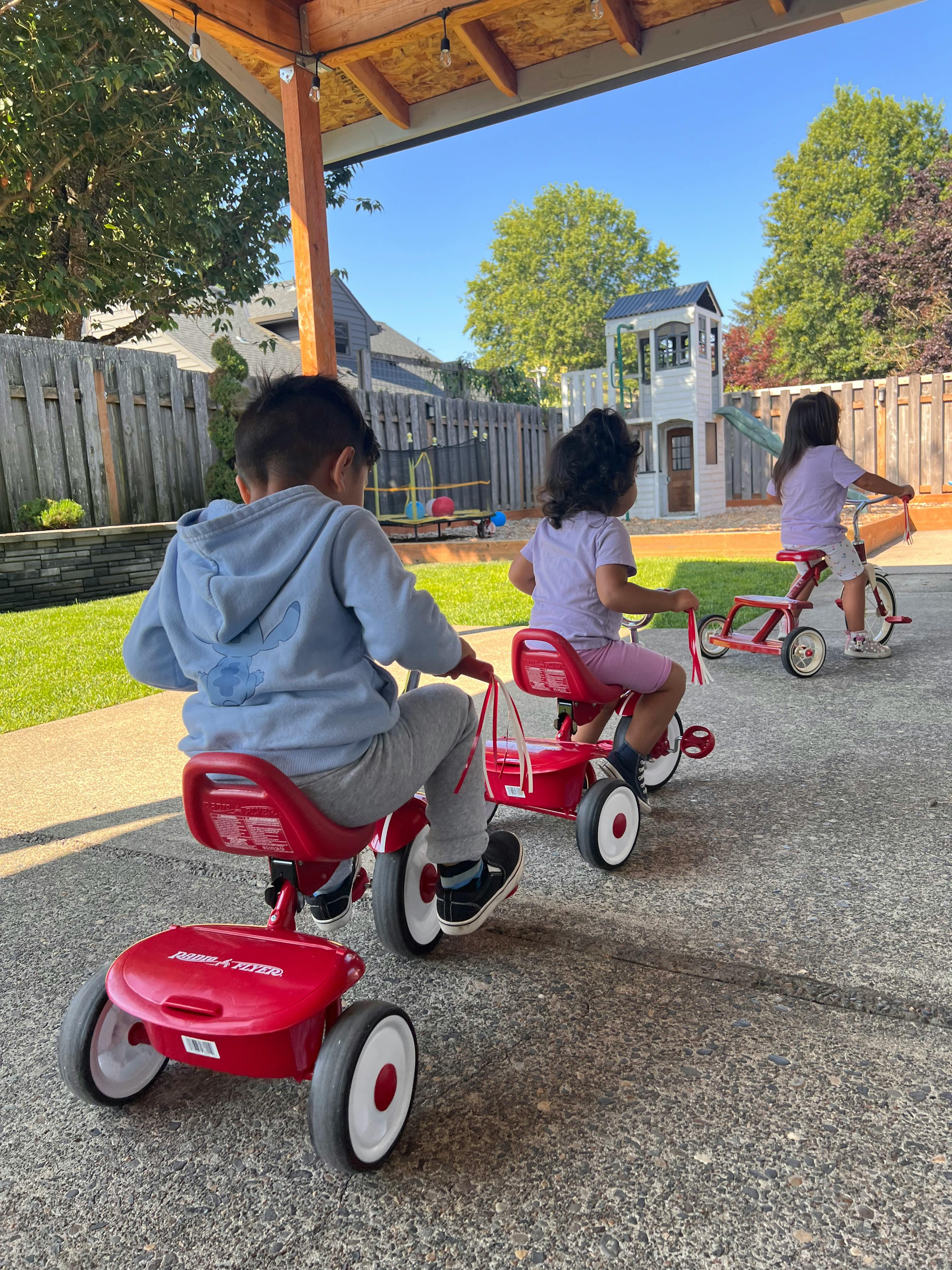 Three children riding red tricycles outdoors