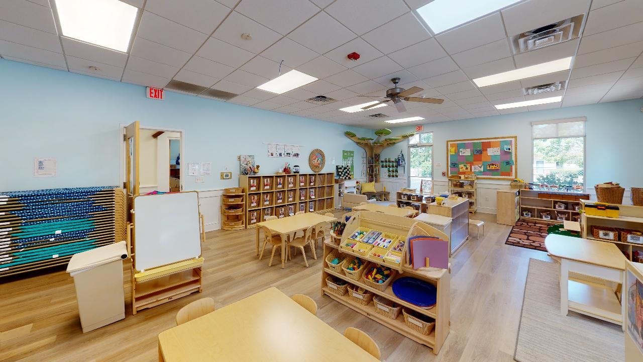 Classroom with small tables and chairs, shelves with learning materials