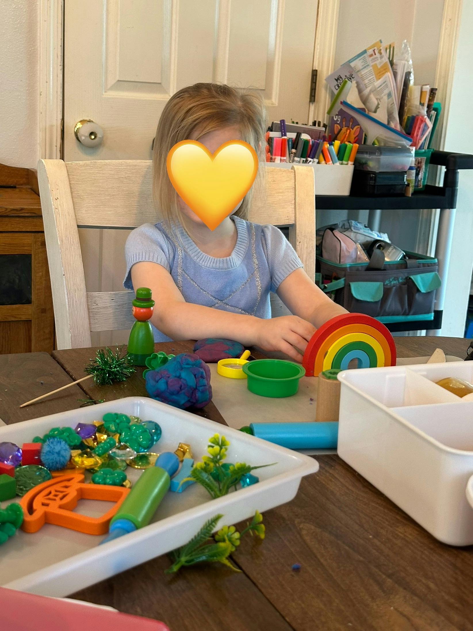 Child at a table with craft supplies and a rainbow toy