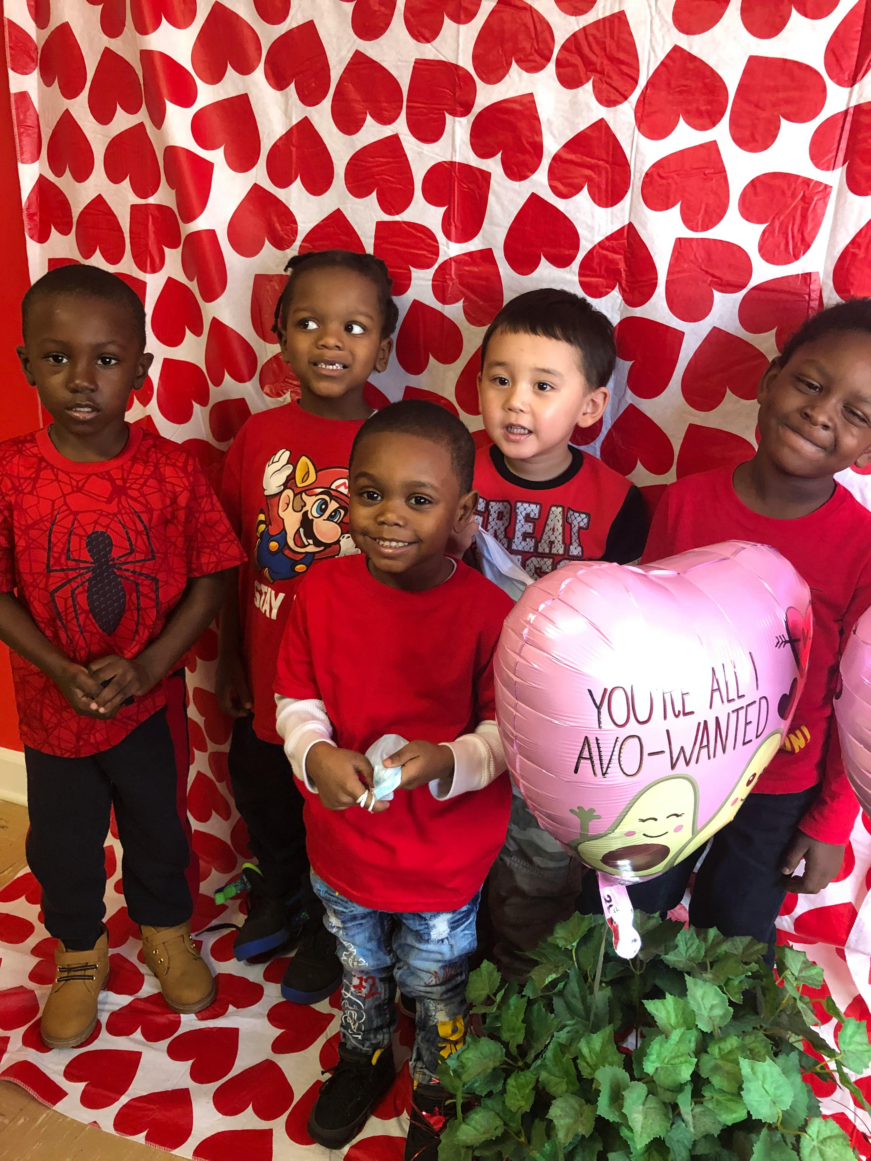 Five children standing in front of a heart-patterned background, red and white background