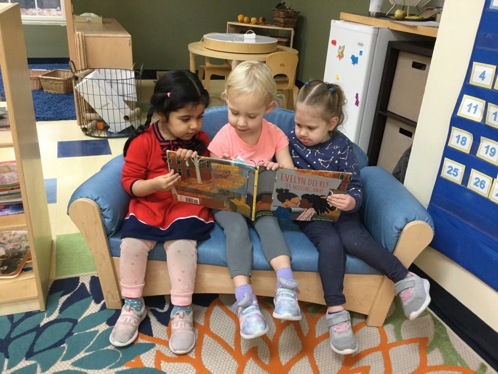 Three children sitting on a couch reading a book together