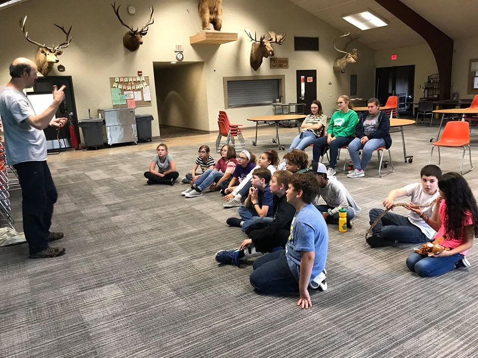 Adult speaking to a group of children and teens sitting on the floor