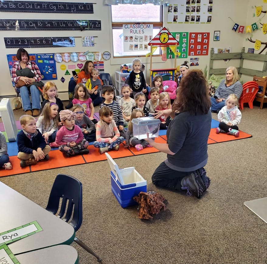 Adult kneeling and showing a container to a group of children