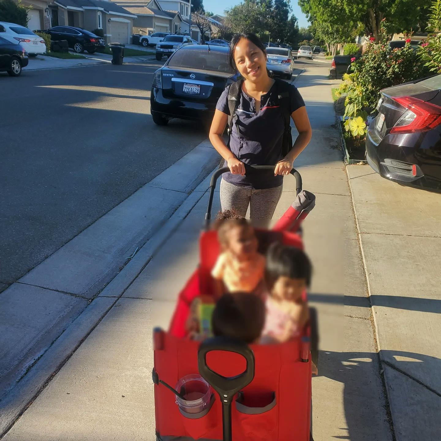 Person pushing a red wagon with multiple children inside on a sidewalk