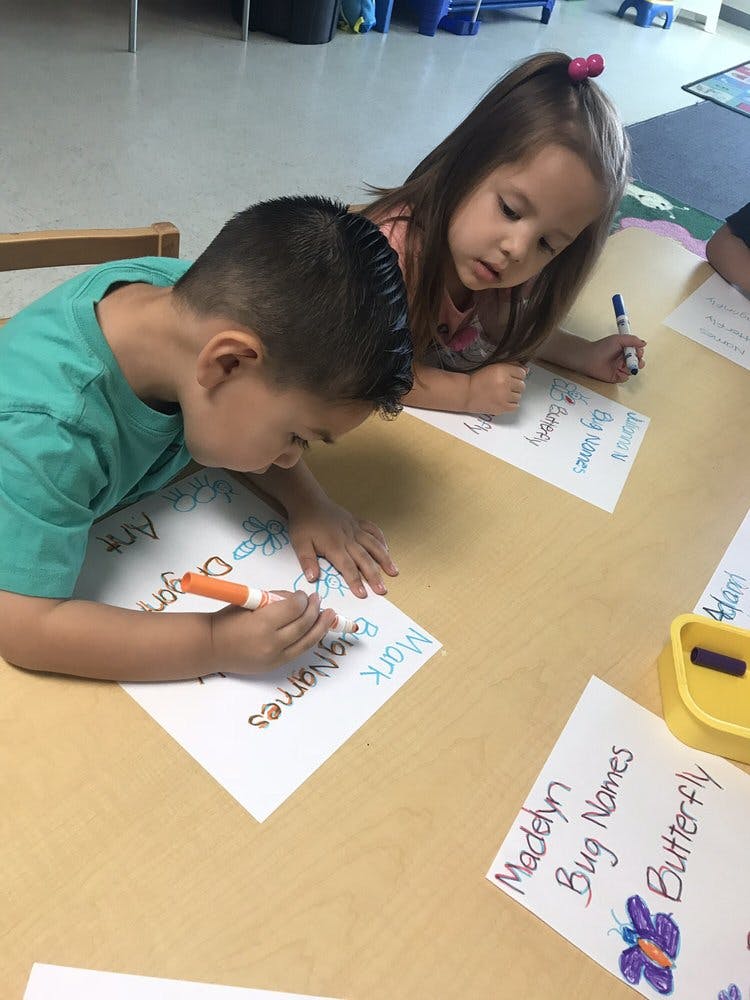 Two children writing on paper at a table