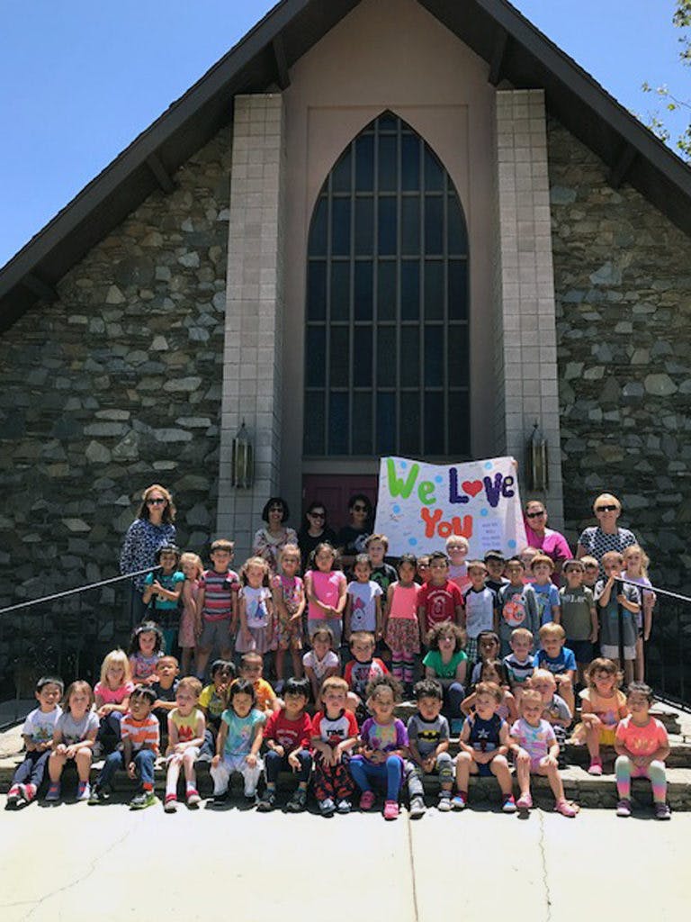 Group of adults and children in front of a building with a banner that says "We Love You"