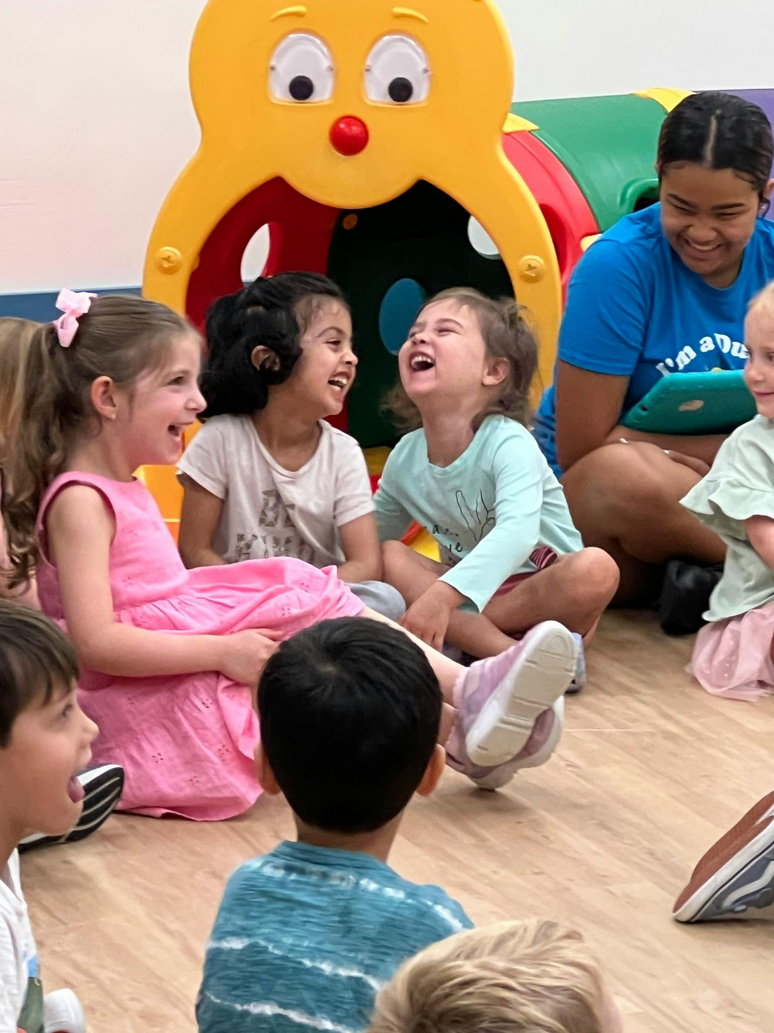 Children sitting on the floor laughing with an adult in the background