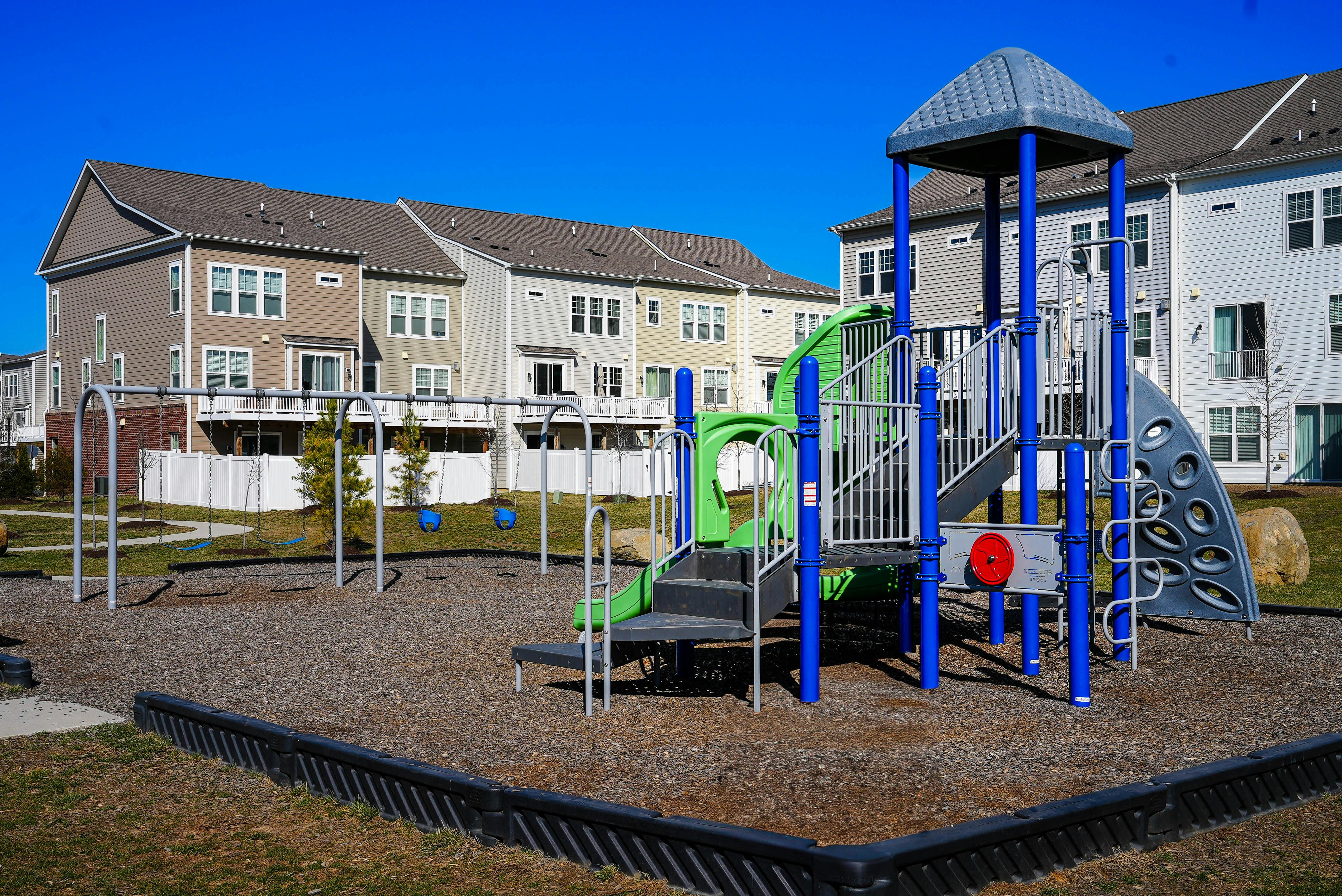 Playground with swings and a slide structure in front of townhouses