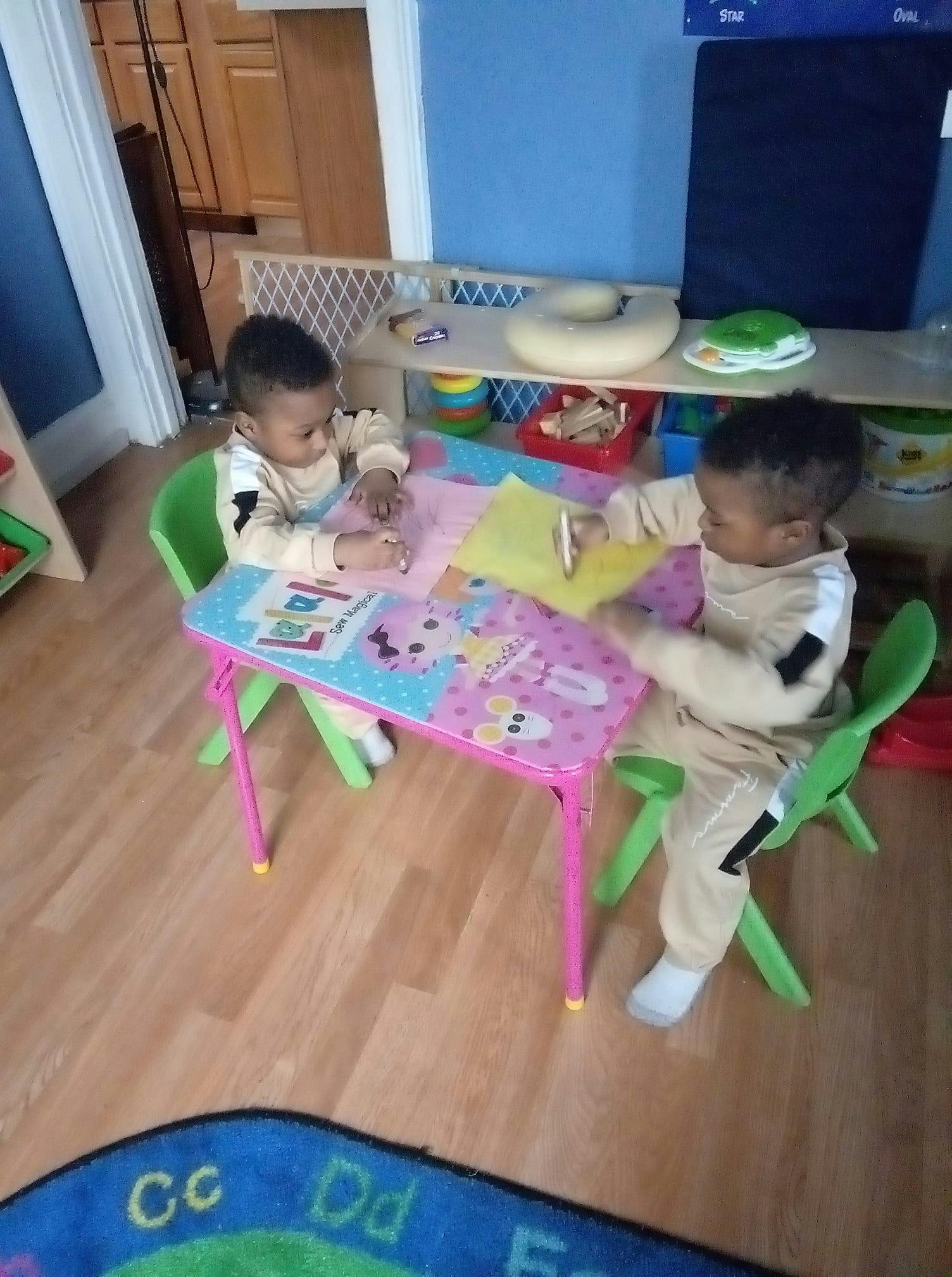 Two children sitting at a small table drawing on paper