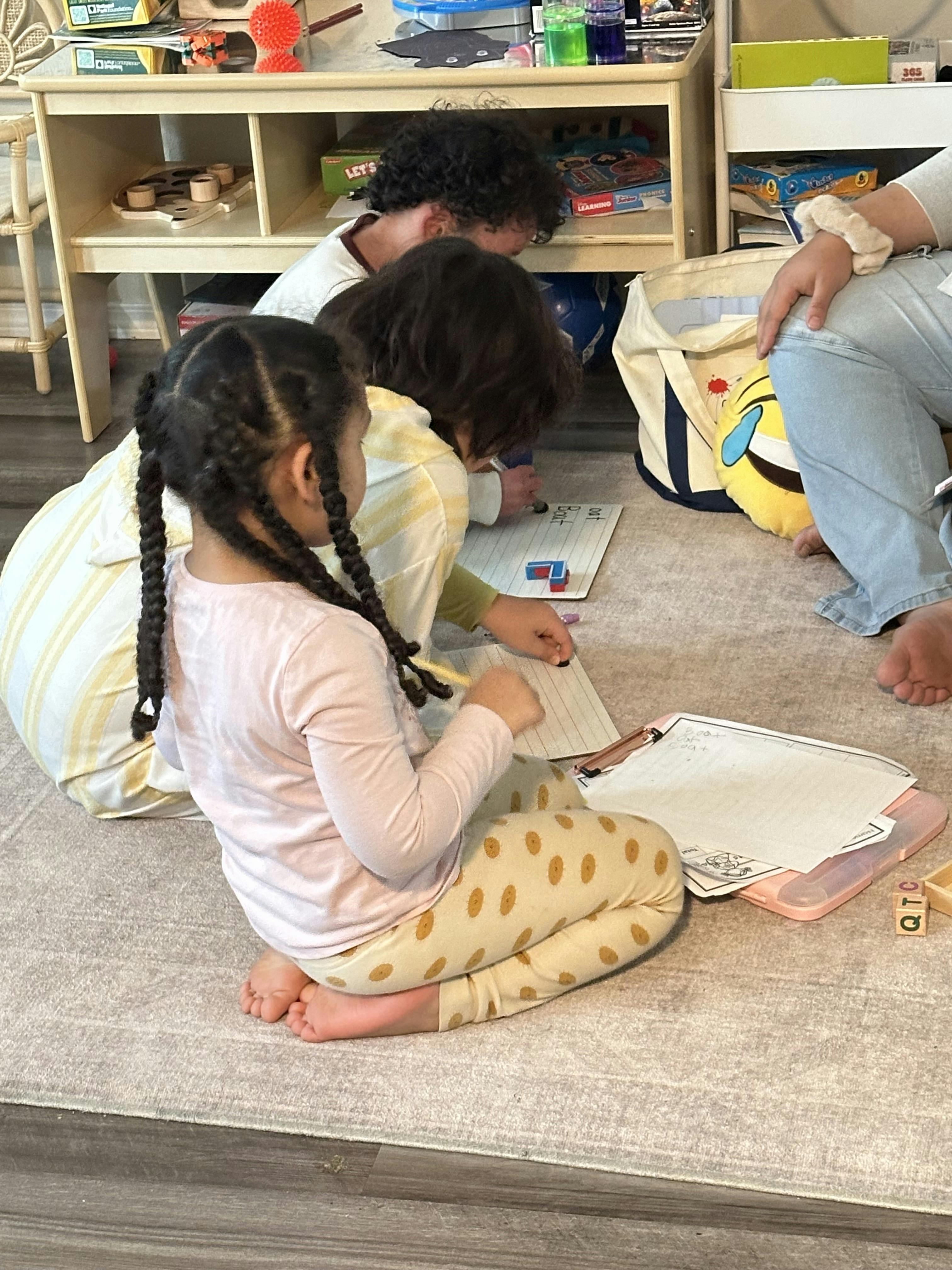 Three people sitting on the floor drawing and writing