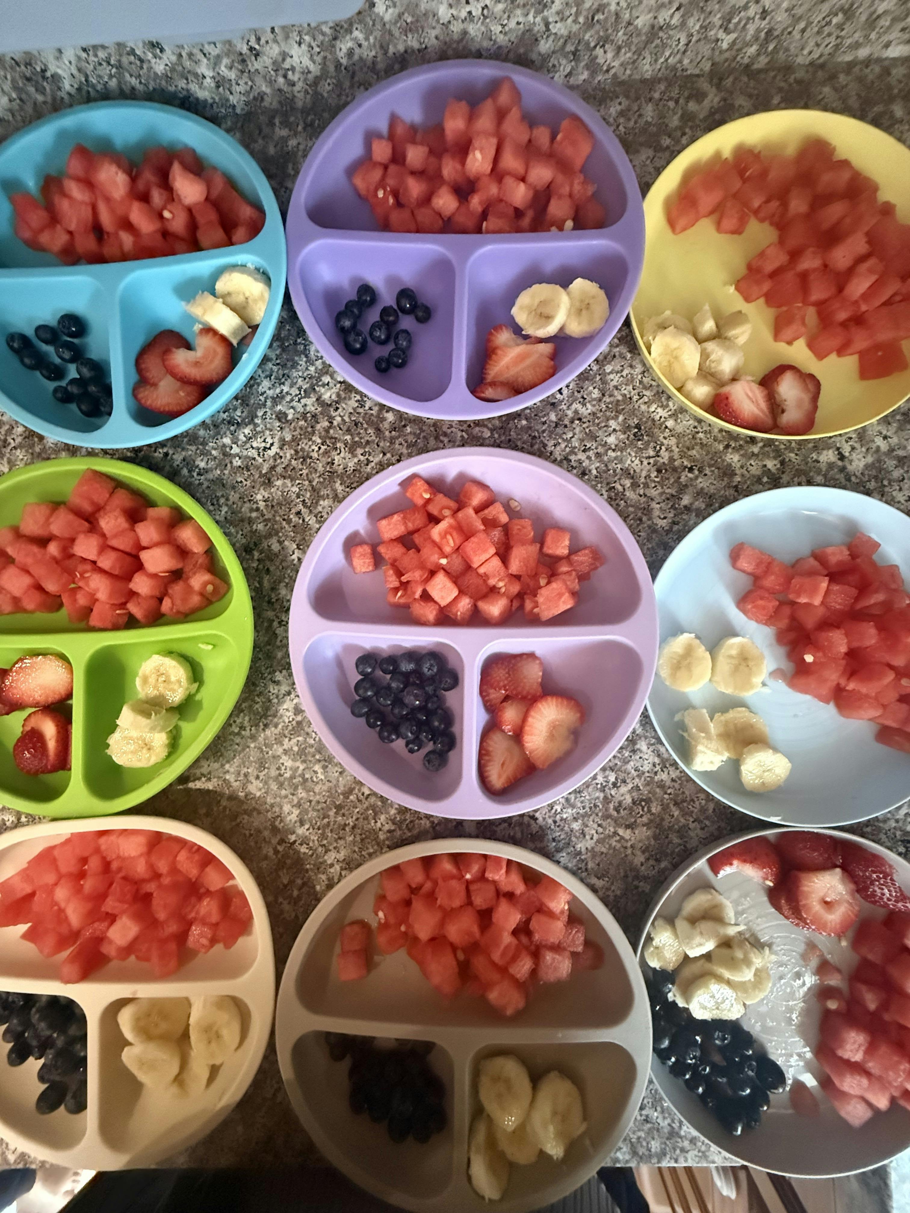 Multiple divided plates filled with portions of watermelon, bananas, and berries