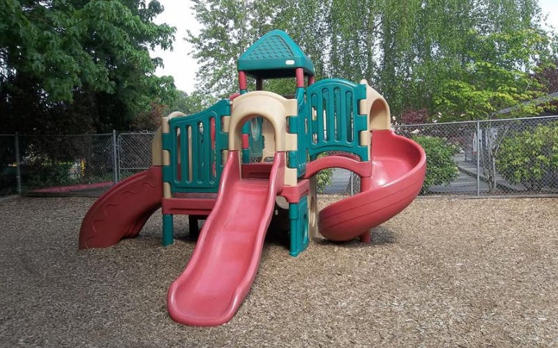 A colorful plastic playground structure with multiple slides on a wood chip surface