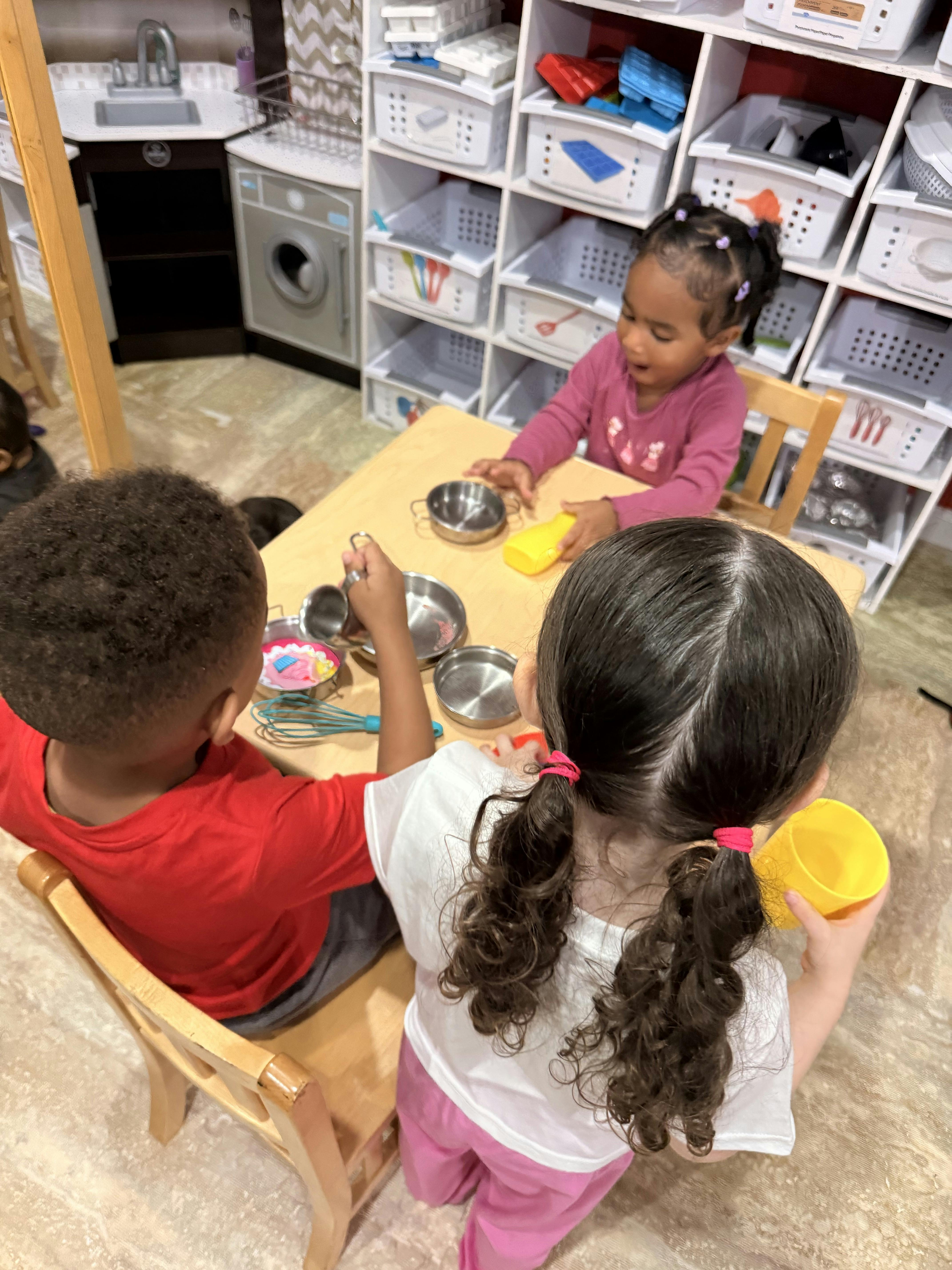 Three children playing with toy kitchenware at a small table