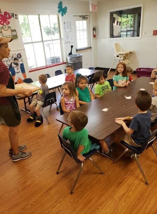 Adult speaking to a group of children seated at tables in a classroom
