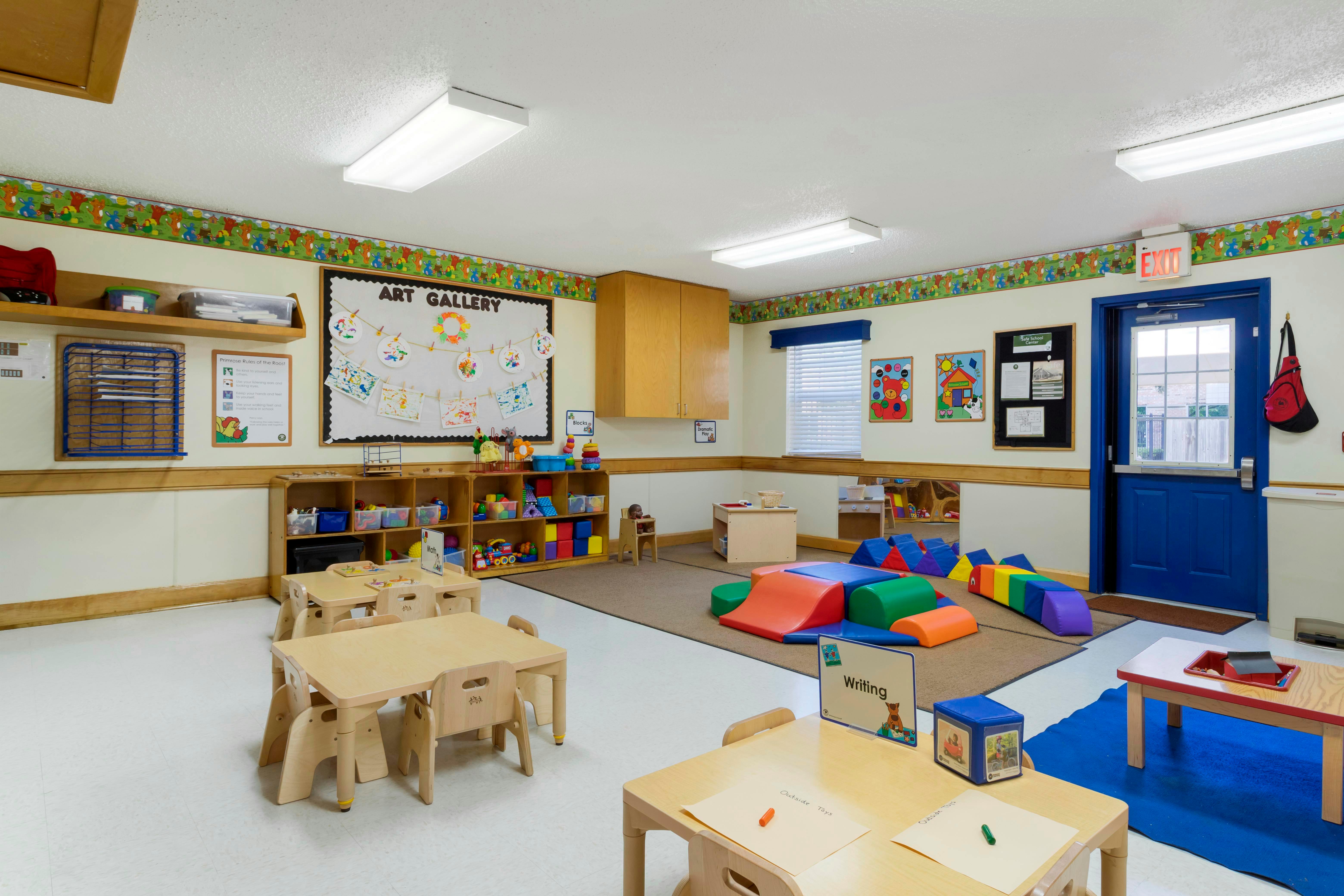 Classroom with tables, chairs, colorful play mats, and an "Art Gallery" board