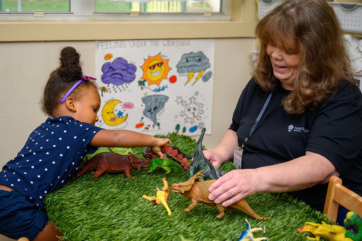 Adult and child playing with dinosaur toys on a green mat