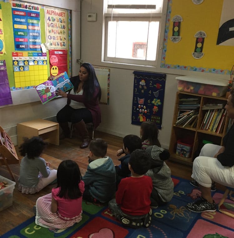 Person reading a book to a group of children in a classroom