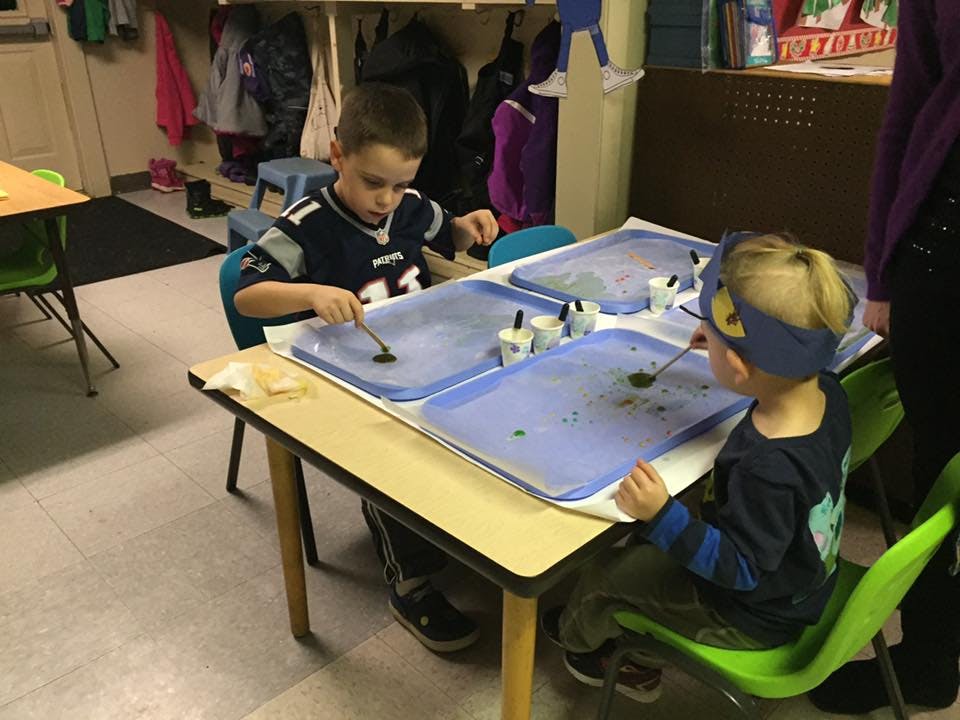 Two children at a table playing with trays of liquid and spoons