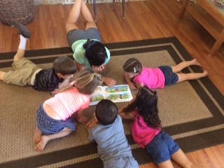 Adult and five children lying on floor looking at a book