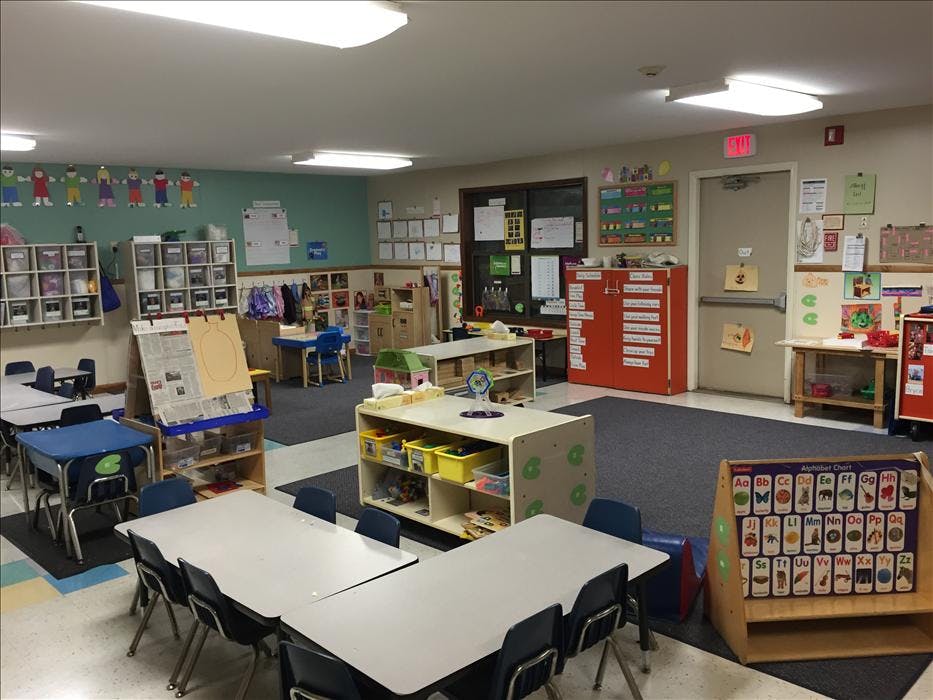 Classroom with tables, chairs, shelving units, and an alphabet chart