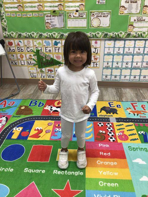 Child holding a First Day of Preschool flag in a classroom