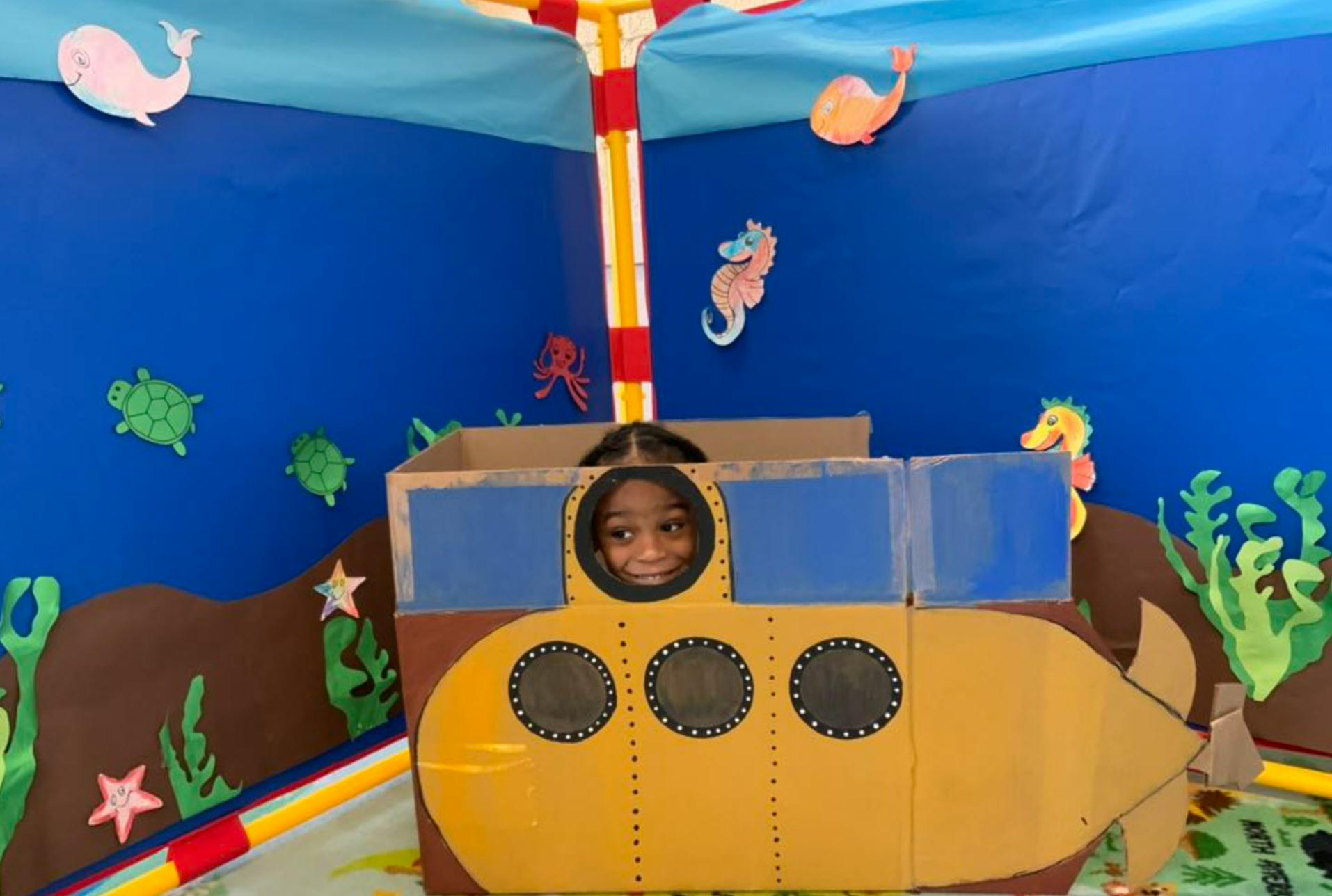 Child peeking from a cardboard submarine