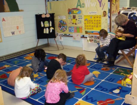 Adult and children sitting on a rug in a classroom