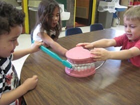 Three children learning to brush teeth with a large dental model