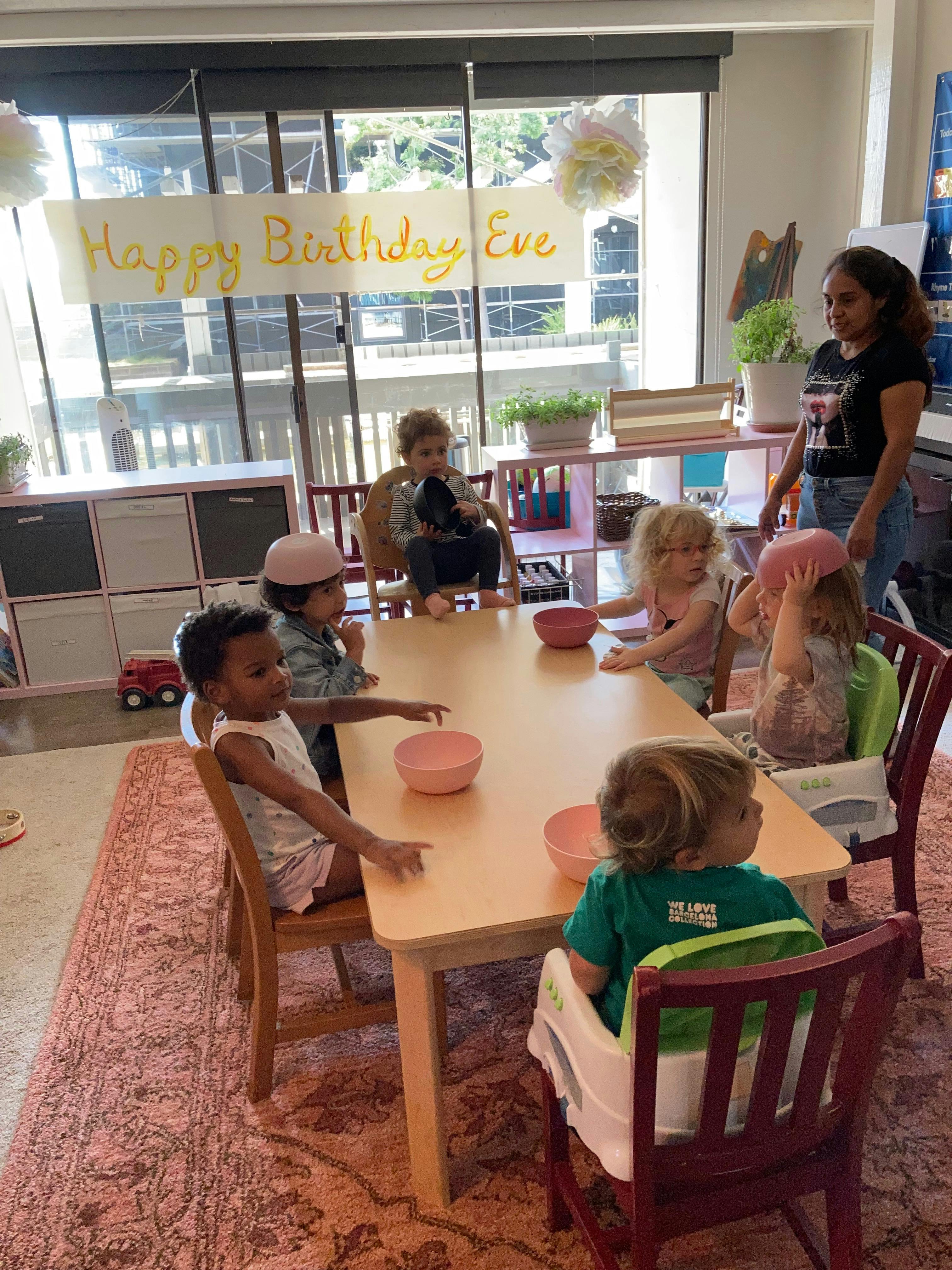 Adult and children sitting around a table with bowls, "Happy Birthday Eve" banner