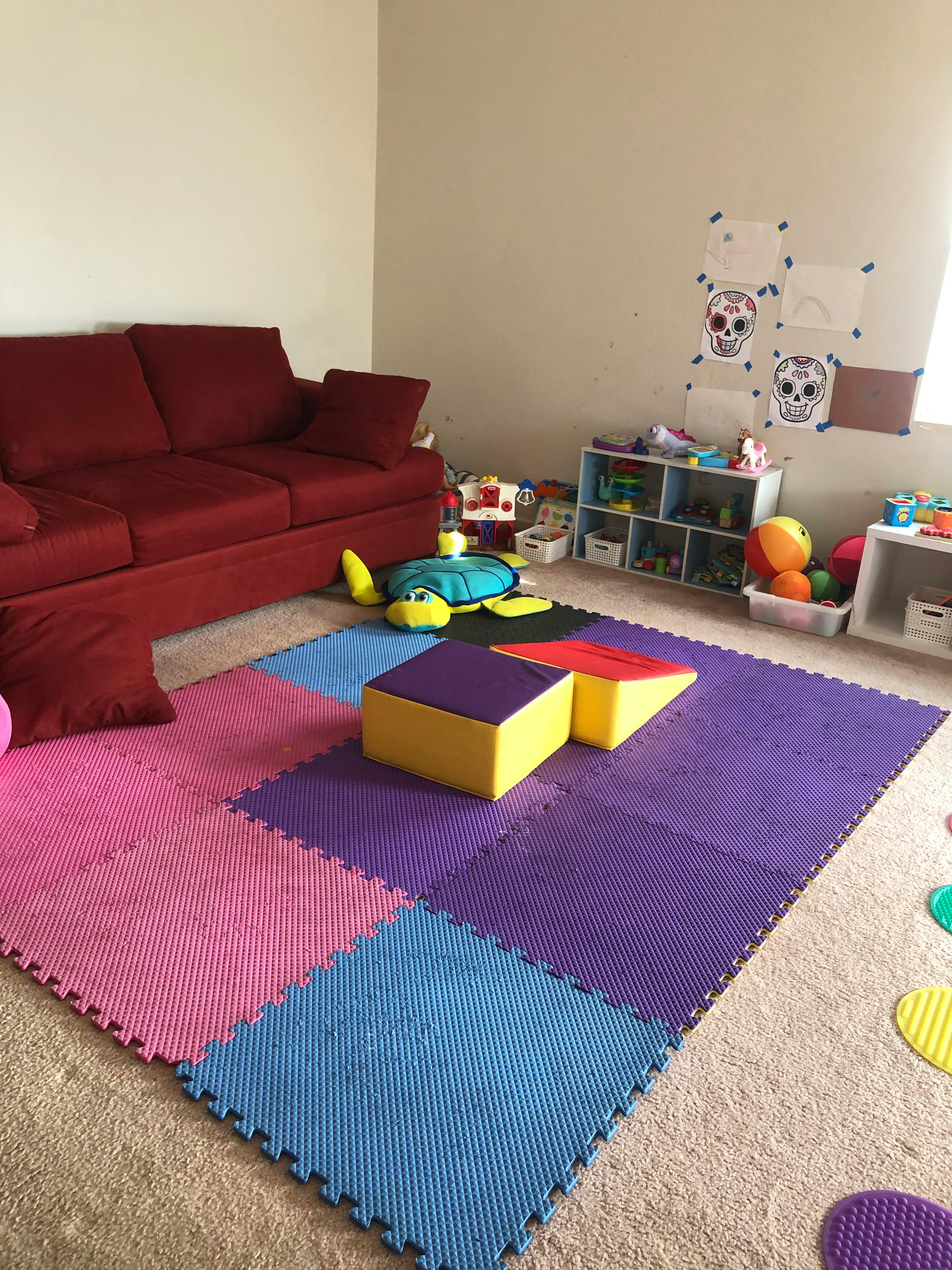 Playroom with red sofa, colorful foam floor tiles, and toys