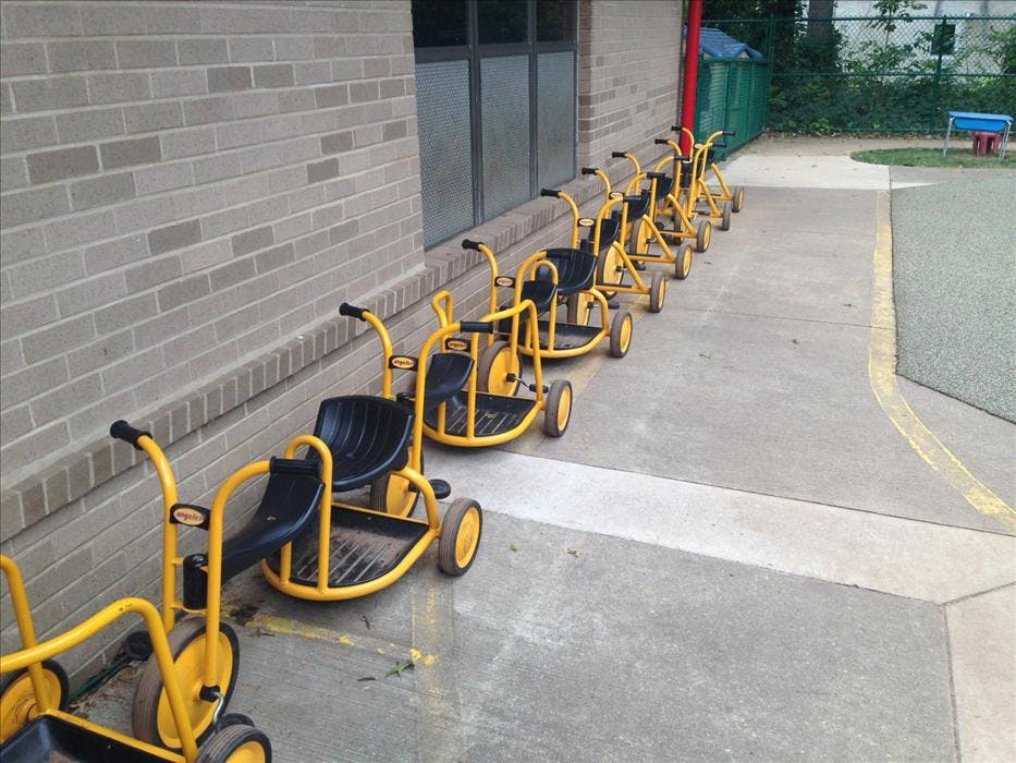A line of yellow and black tricycles for children parked next to a brick building