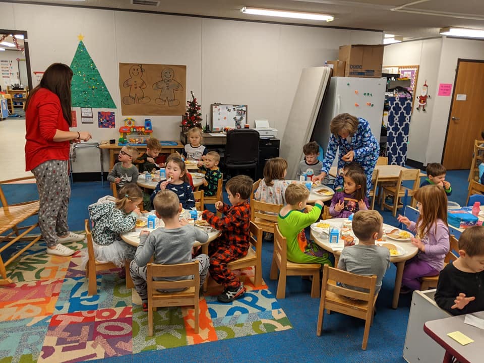 Adults and children gathered around tables in a classroom