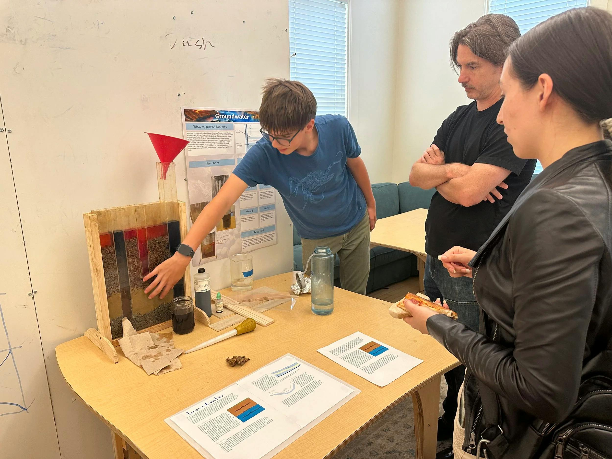A child demonstrating a groundwater exhibit to two adults