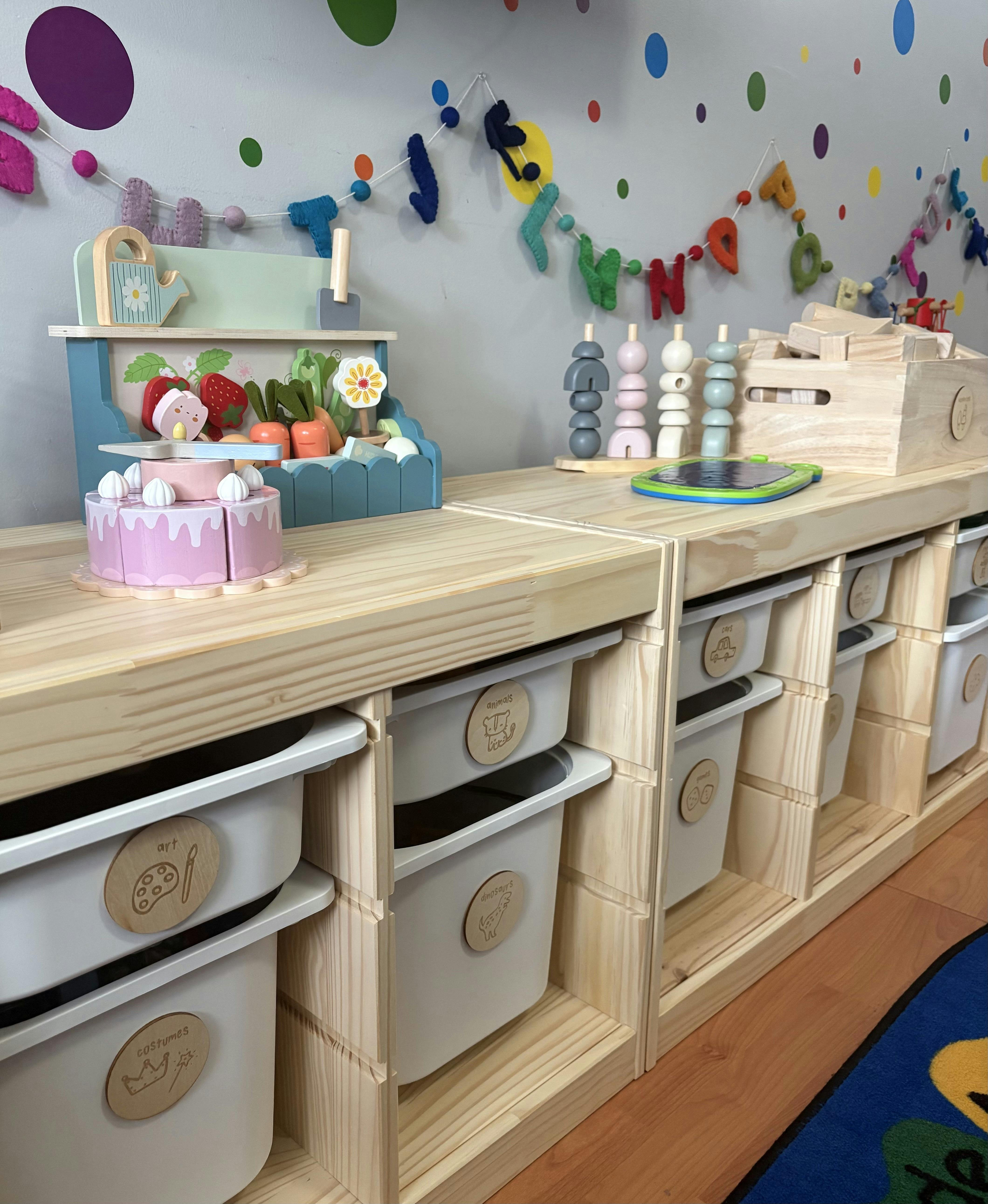 Wooden toy storage shelves with labeled bins and play food in a classroom